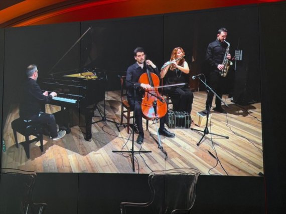 Standbild der Videopräsentation eines Musikvorspiels mit Maestro Luigi Mariani (am Klavier) und weiteren an der Aufführung beteiligten Musikern