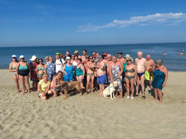 Gruppenfoto der Mitglieder am Strand zusammen mit den zwei Blindenführhunde